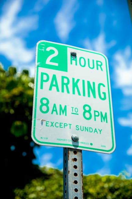 A rectangular illuminated sign mounted on an exterior brick wall indicates 'NO PARKING IN ALLEY' with a red circle and slash over a blue and red parking symbol. The sign features purple border lines a